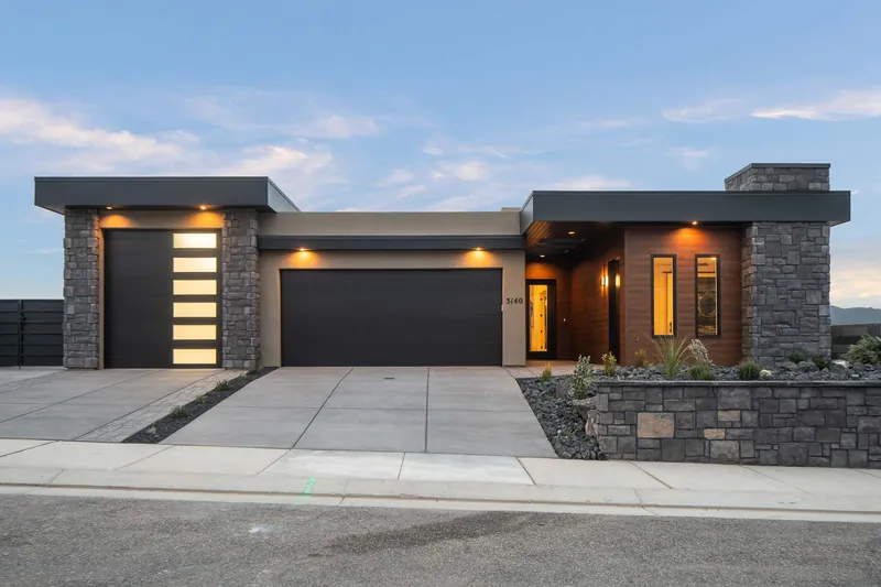 Modern single-story home at dusk, with a stone wall and lit windows