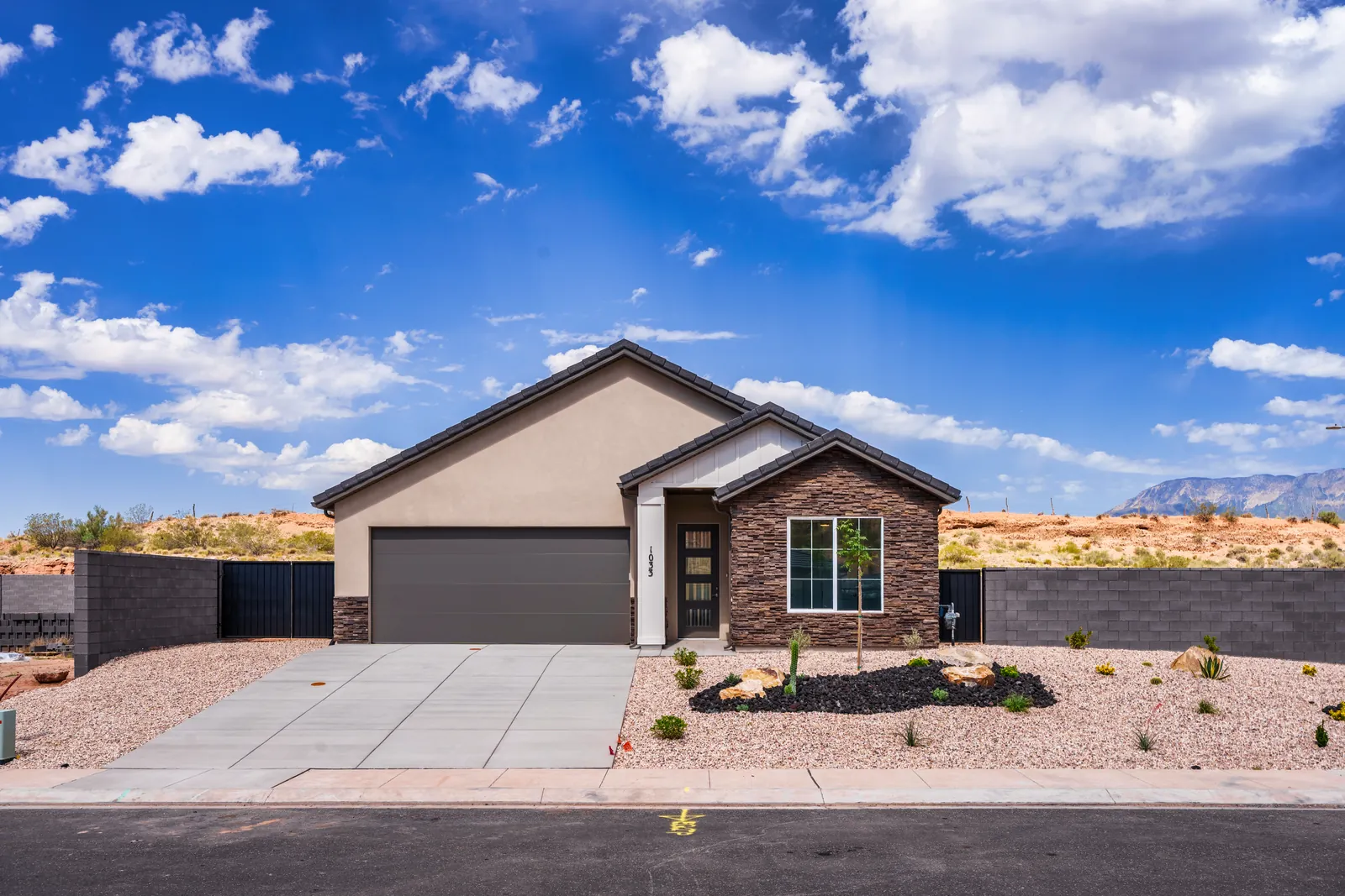 Front of a single-story home with a stone-faced wing and a deep blue sky