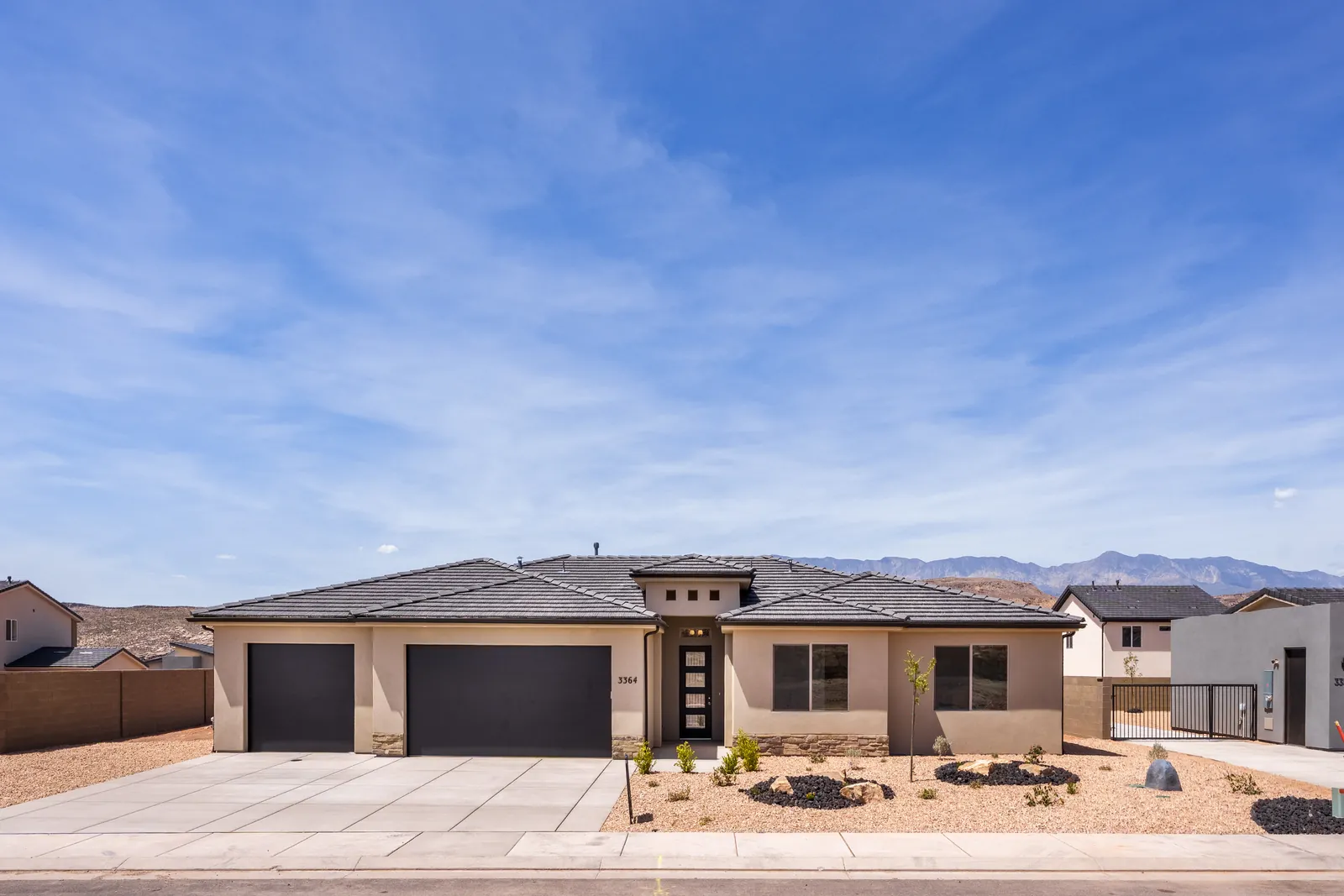 A single-story home with a long driveway and mountains behind